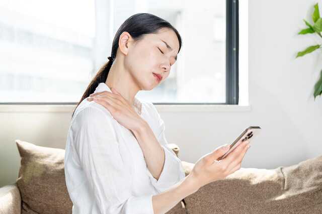 スマホを触りながら肩をおさえる女性